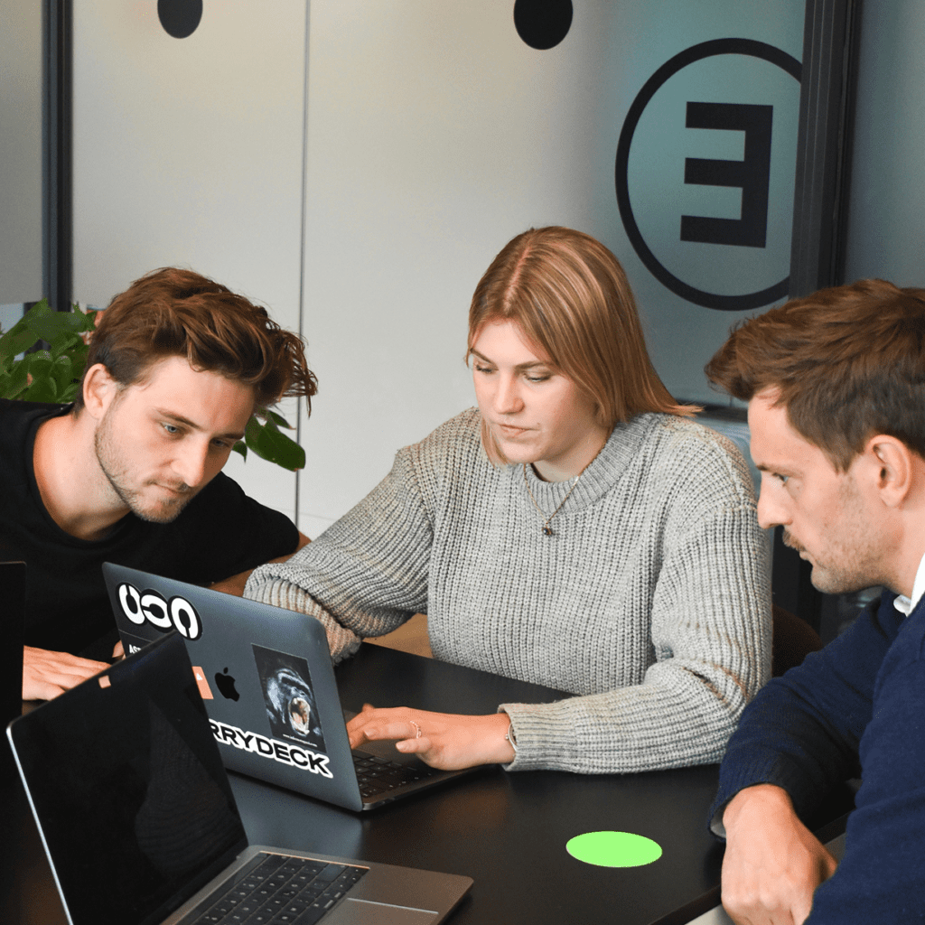 Three colleagues collaborating over a laptop in a modern office.