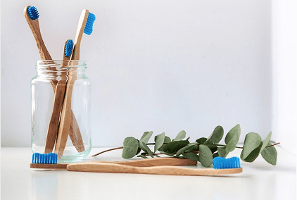 Toothbrushes in a jar with eucalyptus on a wooden tray.